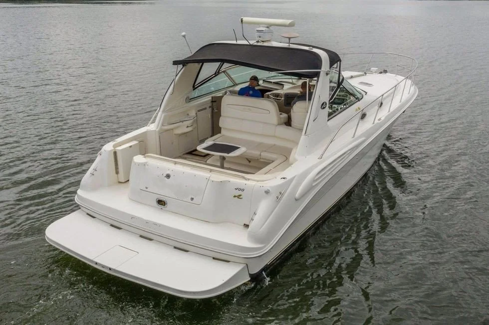 White motor yacht on water with seating area and black canopy, person sitting at the helm.