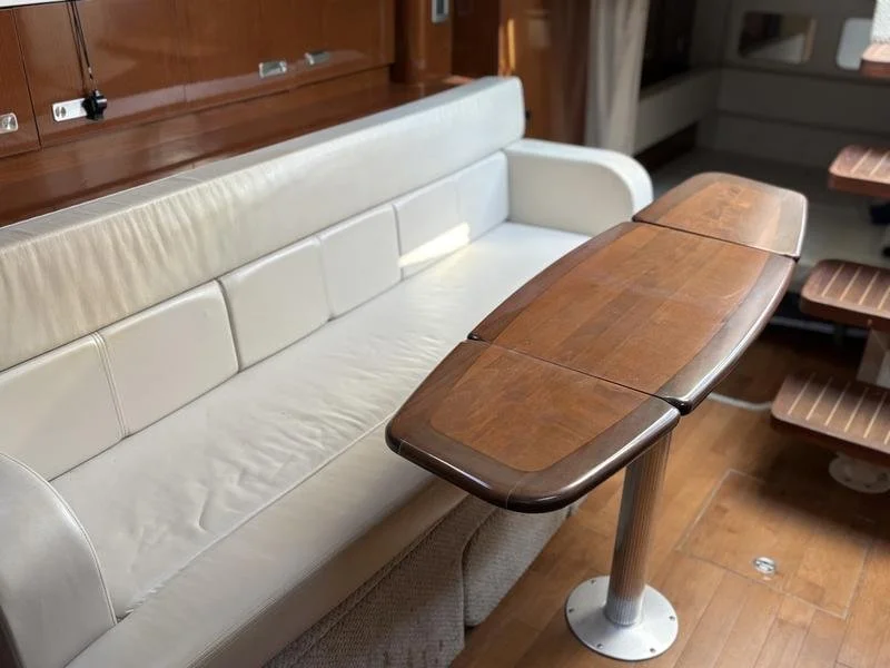 A white leather bench seat with a foldable wooden table in a boat or yacht interior.