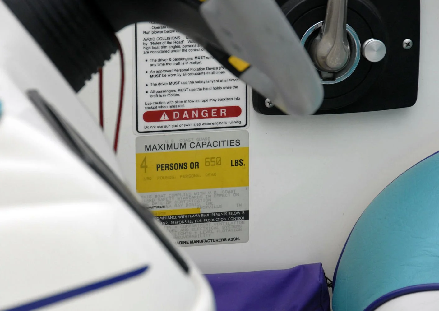 Close-up of a boat's control panel showing safety and capacity labels, including maximum capacity of 4 persons or 650 pounds, and a warning sign in red.