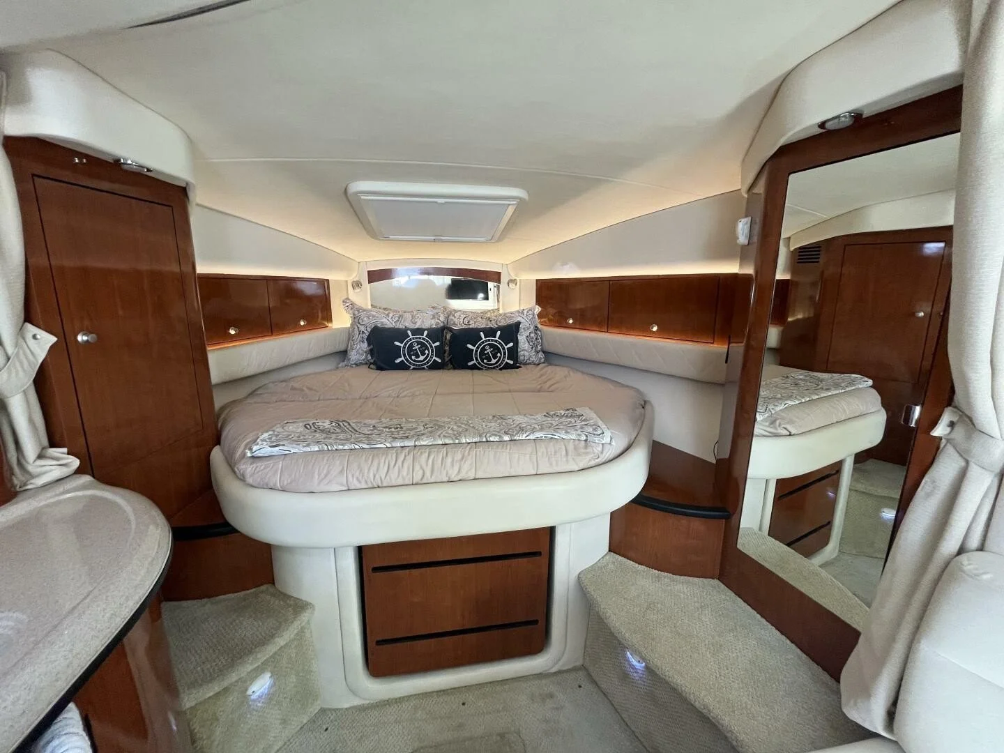 Interior on Sea Ray 340 Sundancer, showing forward vee-berth sleeping area, a large bed, wooden storage cabinets, and a small hall with a mirror and a bed to the side, in neutral tones.