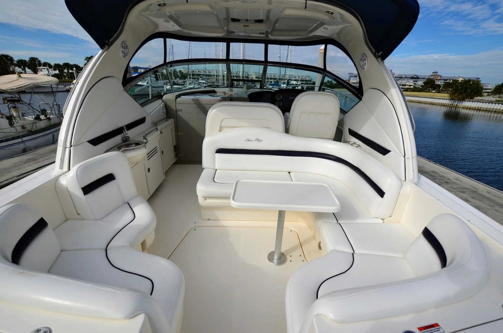 White motorboat interior with cushioned seating, a small table, and a view of a marina with boats and water outside.