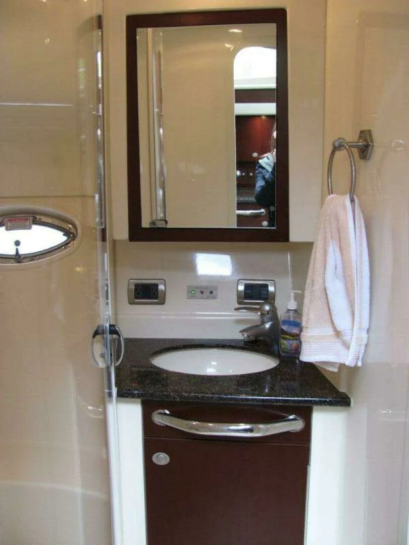 Boat's bathroom vanity with a dark countertop, oval sink, mirror cabinet, towel ring with a white towel, and soap dispenser.