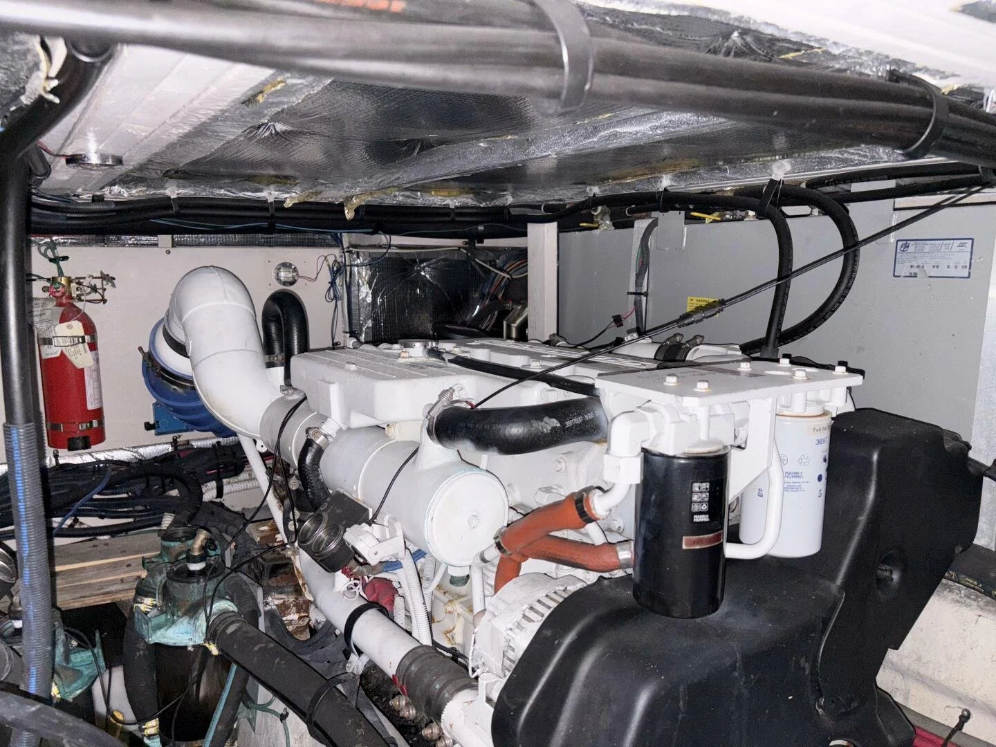 Marine engine room with white engine, black hoses, fire extinguisher, and various mechanical components. Cummins engines. Sea Ray yacht.