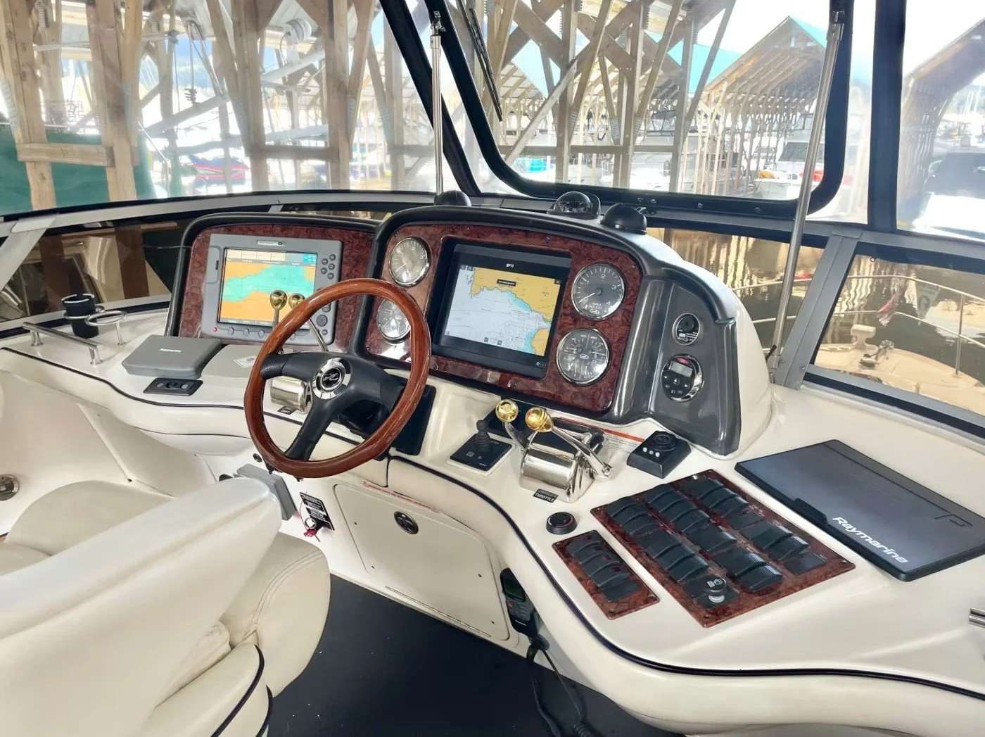 Interior view of a boat's dashboard featuring navigation screens, gauges, and controls with a wood steering wheel.