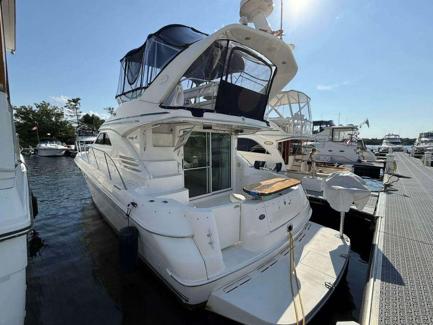 Aft cockpit view of a white Sea Ray 400 Sedan Bridge yacht docked at a marina with a floating dock, surrounded by other boats under a sunny sky.