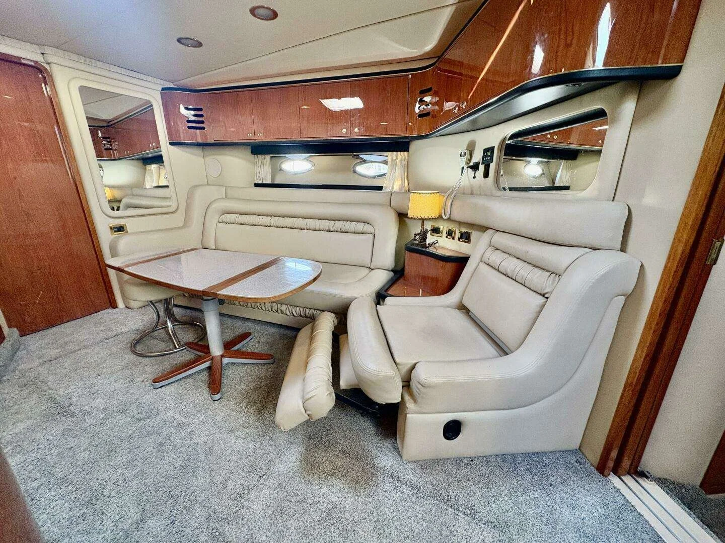 Interior of a luxury yacht with cream leather seating, a wooden table, built-in mirrors, port-light windows and cherry wood cabinetry. Sea Ray 460 Sundancer. 