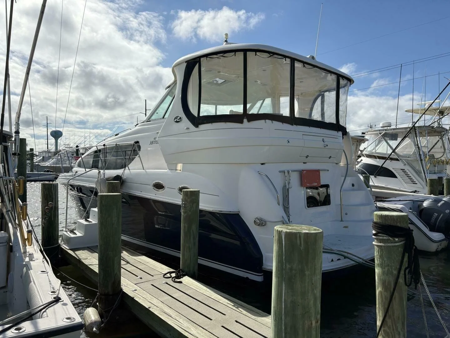 White motor yacht docked at a marina with boats, wooden dock, and cloudy sky in the background.