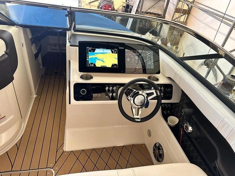 The image shows the dashboard and helm of a modern motor yacht with navigation screens, steering wheel, and control panels. The interior features wood flooring and a sleek white design. Sea Ray 280 SLX with Mercruiser controls, Simrad chartplotter.