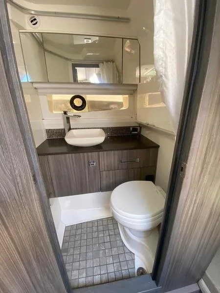 Small bathroom with a compact sink, a mirror, a cabinet, and a toilet, in a space-efficient design.
