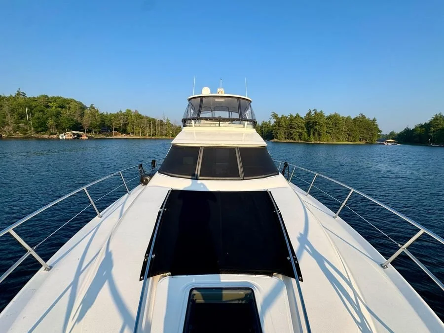 View from the front of a white yacht cruising on a lake with trees on the shoreline and a clear blue sky. Sea Ray 480 Sedan Bridge.