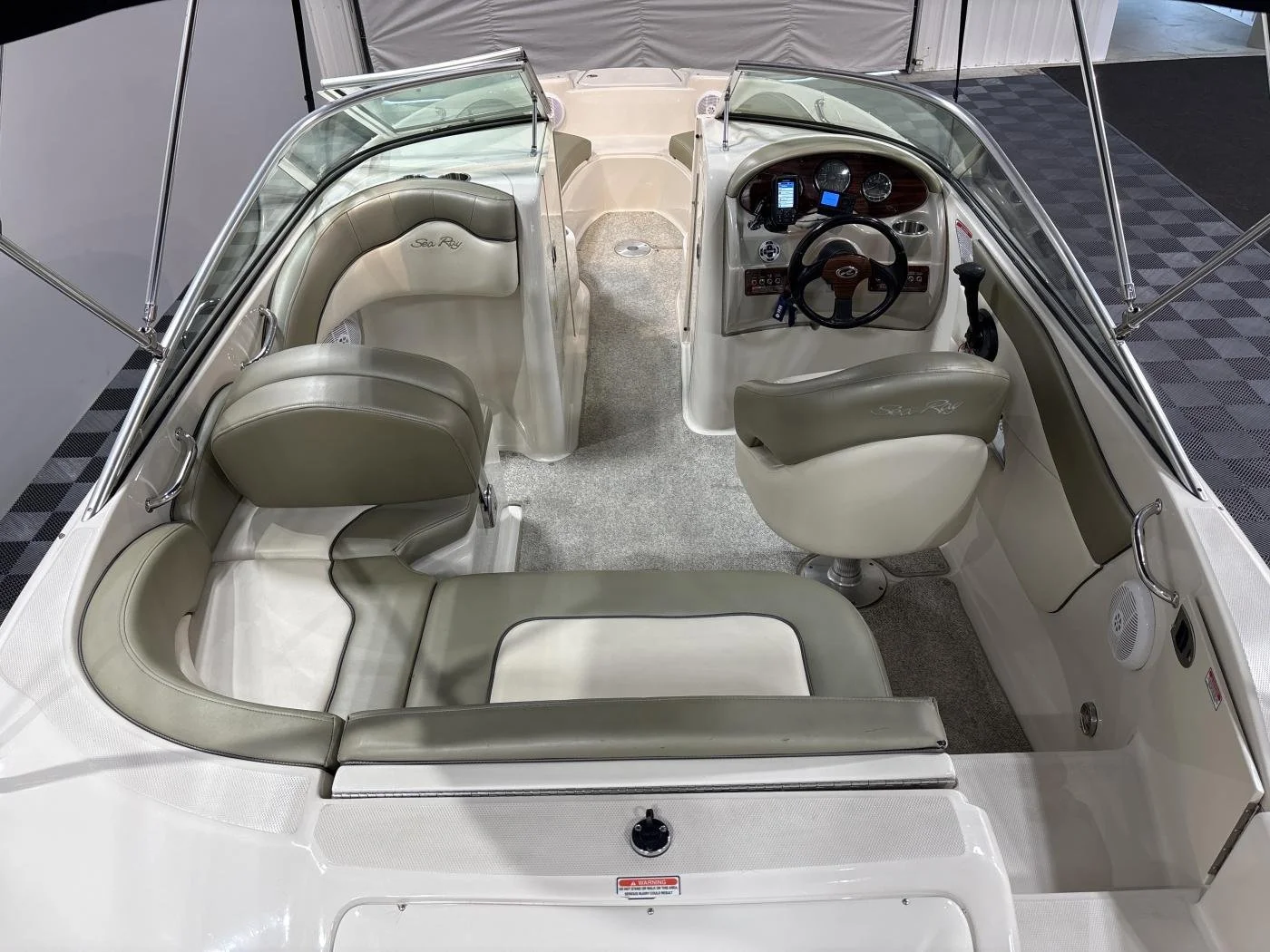 Interior of a small pontoon boat with beige and tan cushioned seats, a steering wheel, and dashboard with gauges and a phone holder