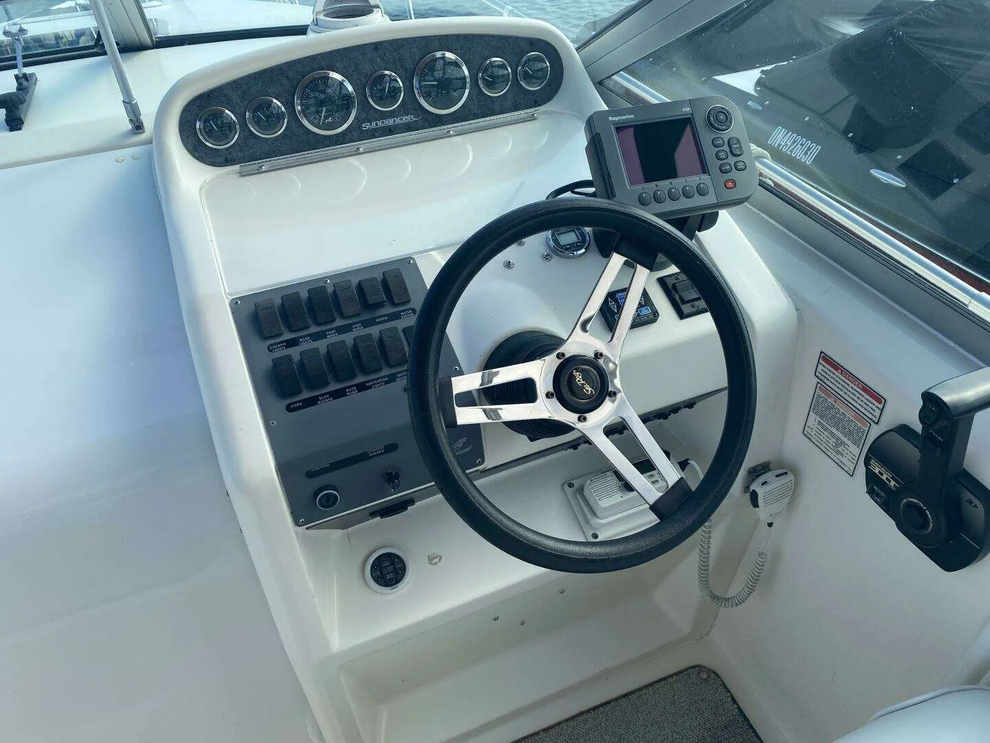 Boat steering console with a black wheel, electronic navigation equipment, and various control switches and gauges. Helm on Sea Ray 270 Sundancer.