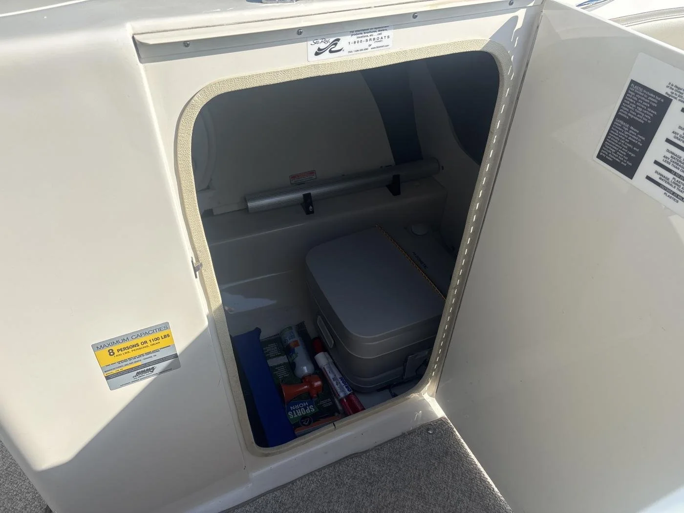 Open storage compartment on a boat showing a first aid kit, a bottle of sunscreen, and some bottled items inside.