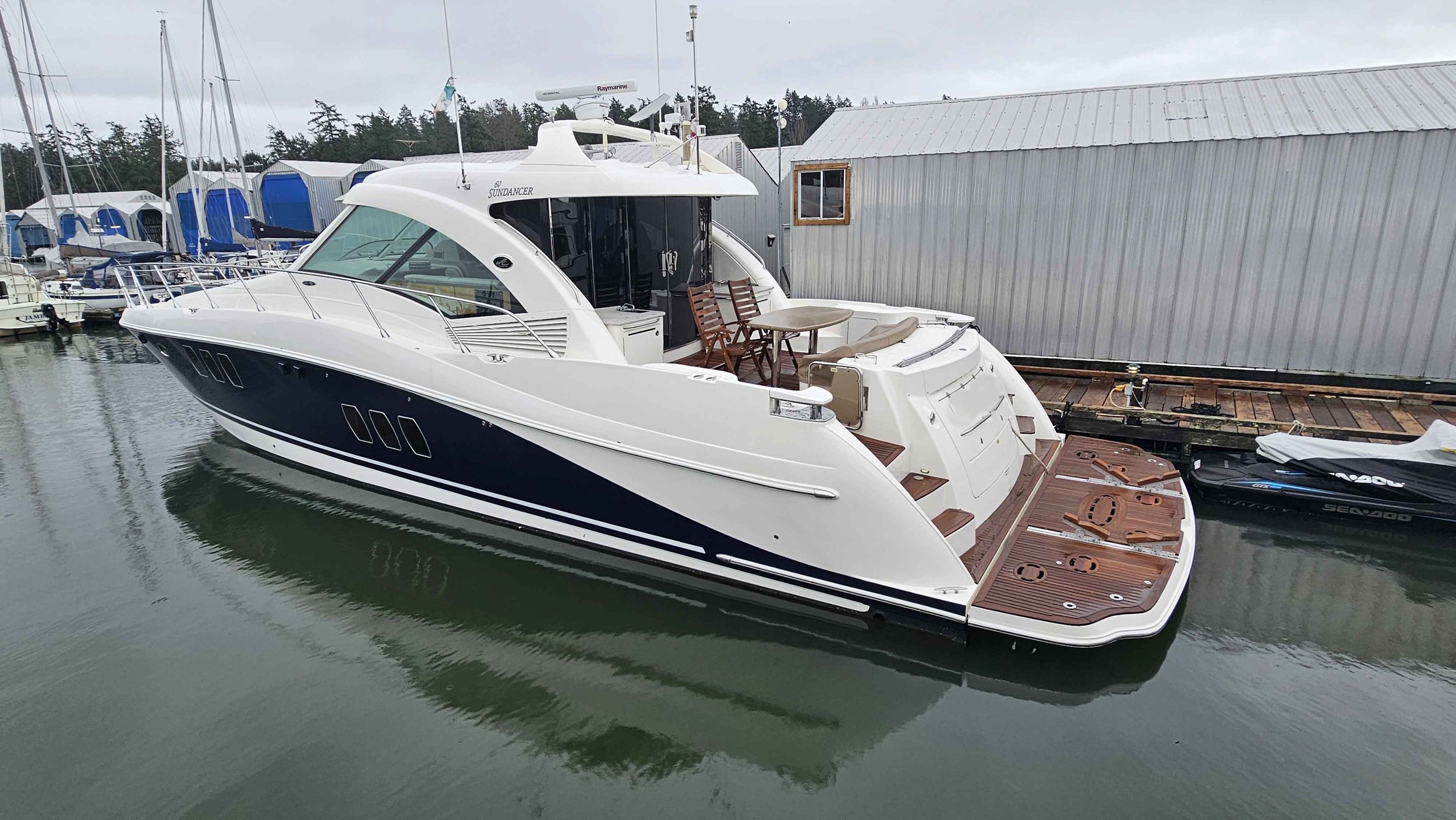 Large white and navy yacht docked at a marina with other boats and a gray building in the background. Sea Ray 60 Sundancer boat.