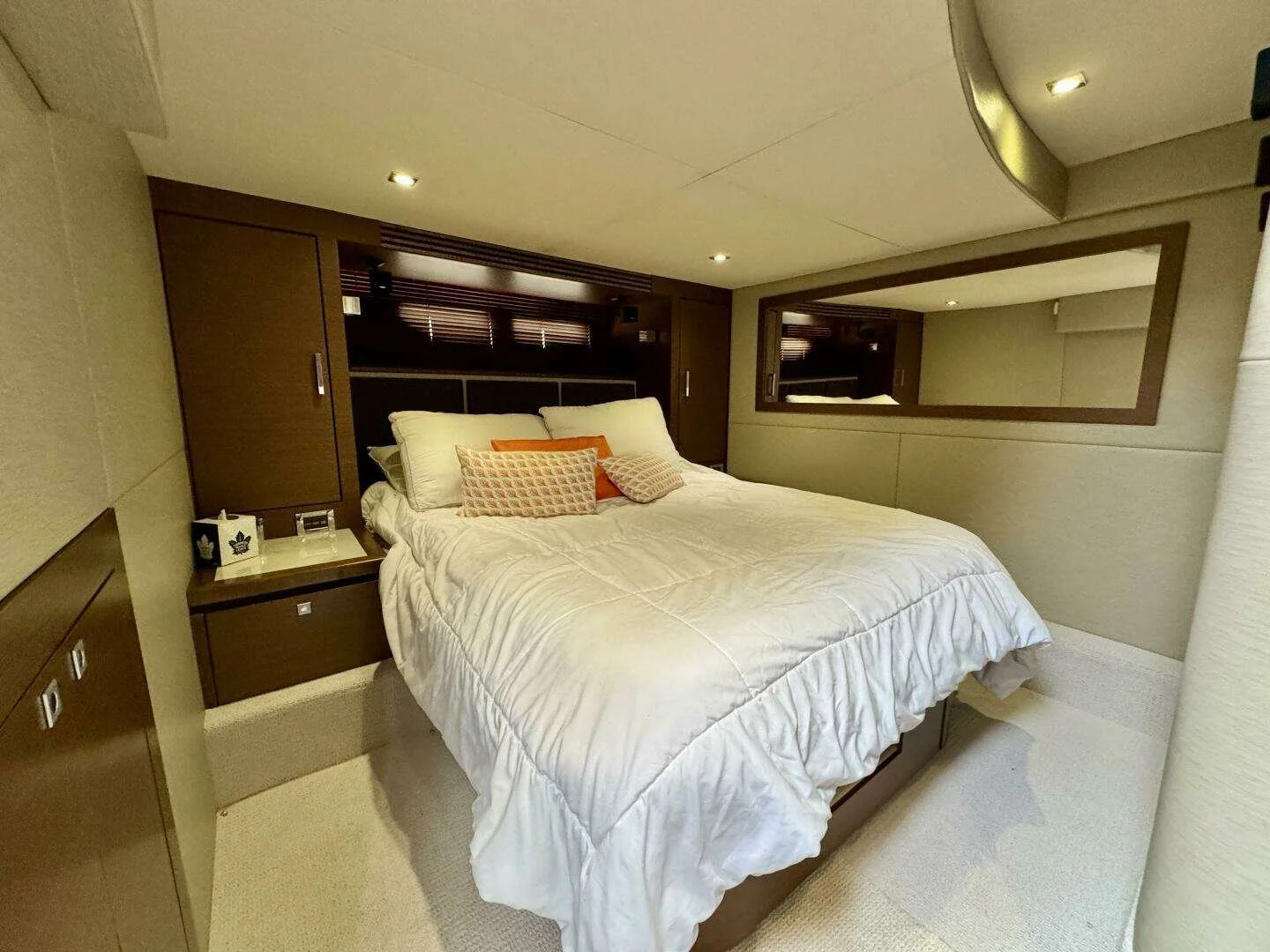 Luxury yacht bedroom with a white bed, decorative pillows, wood paneling, and large mirror. Sea Ray boat.