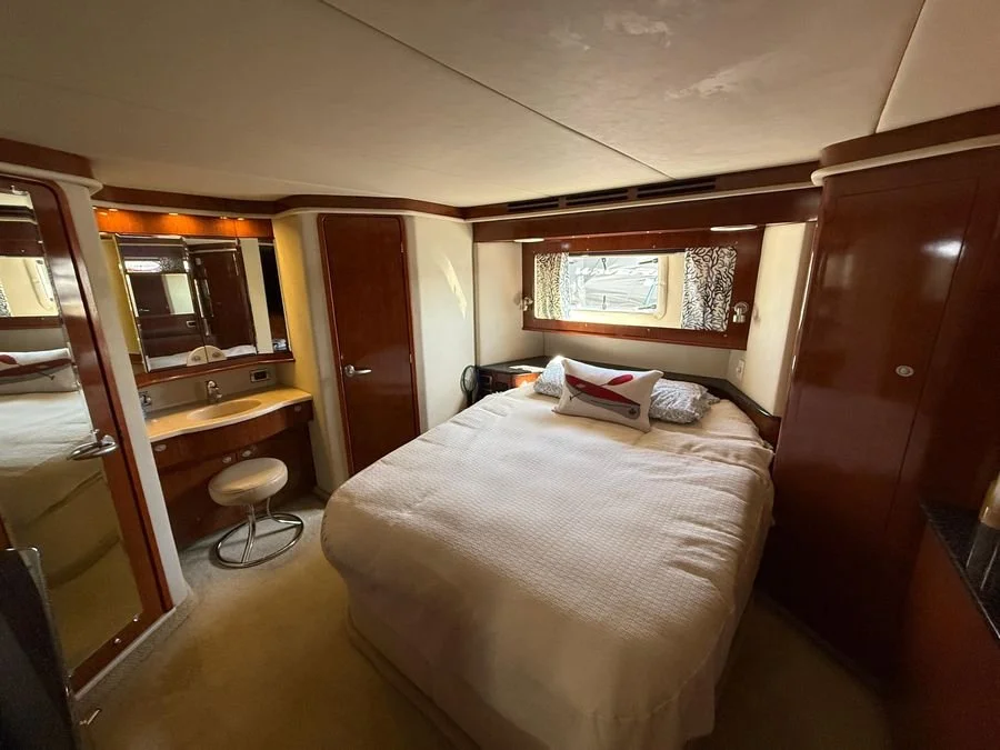 A cozy bedroom in a Sea Ray boat or with a bed, pillows, a small window, a vanity with a stool, and wooden cabinets.