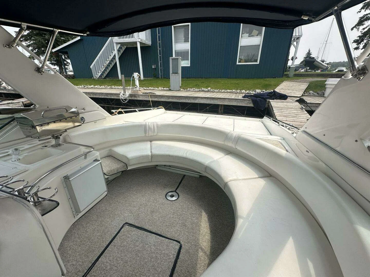 View from inside a boat showing white cushioned seating area, with a dock and grassy area with a blue building and boats in the background. Sea Ray 380 Sunsport.