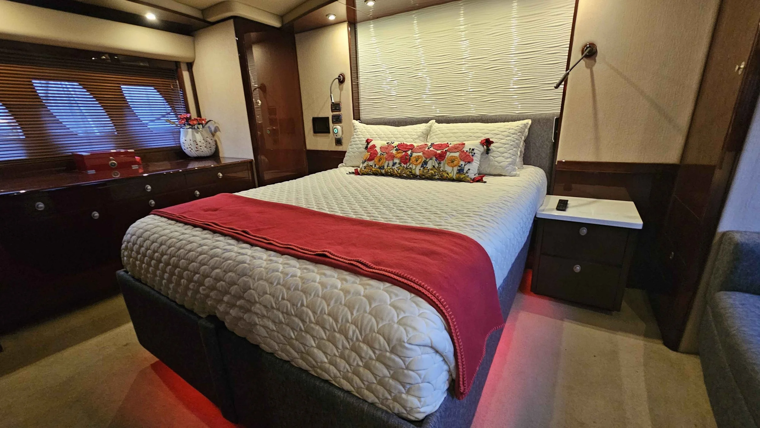 A Sea Ray yacht's master bedroom, with large bed, bright colored coverings, nightstand, with windows and wood mini blinds.