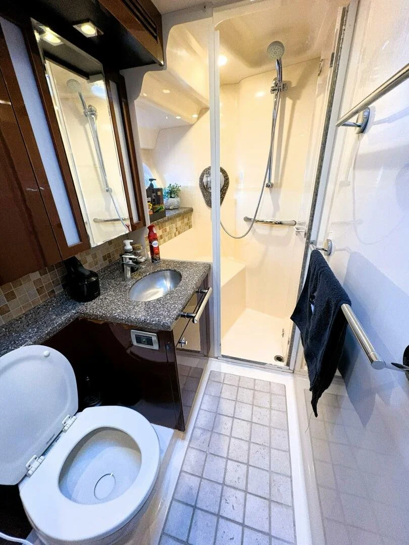 Bathroom / head on a Sea Ray yacht, with a toilet, dark wooden cabinet with a granite countertop, small sink, mirror, shower with glass door, towel racks with black towels, and decorative items including a plant and heart-shaped ornament.