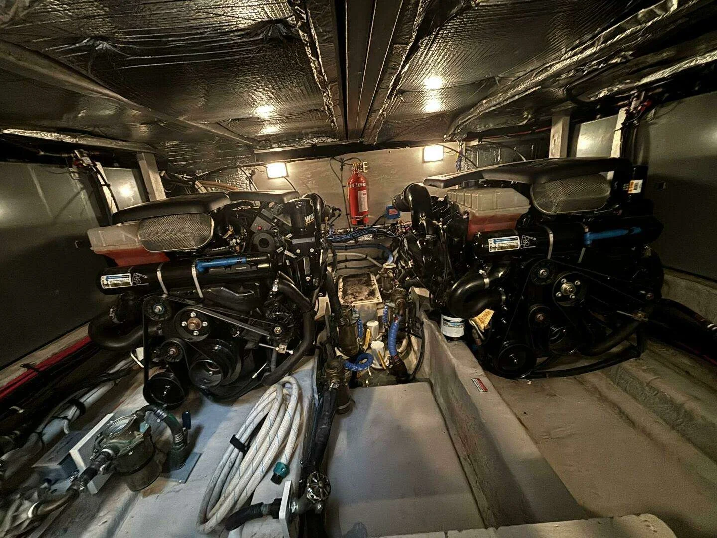 Two Mercruiser marine engines in a Sea Ray yacht, with a fire extinguisher mounted on the wall in the background.