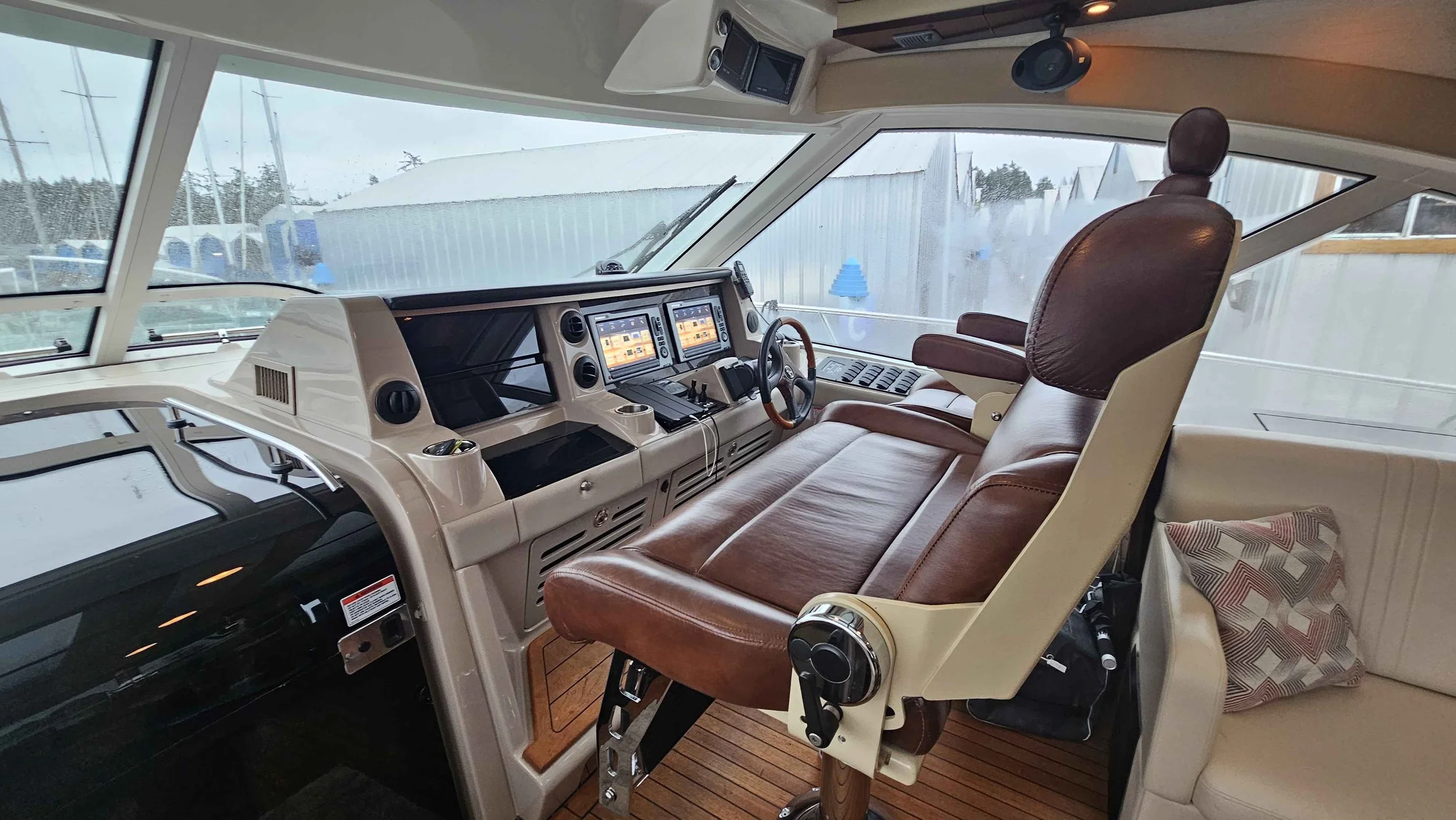 Boat cockpit with large windows, multiple screens, controls, and brown leather captain's chair.