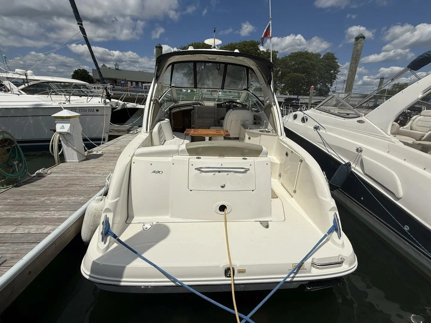 White motor yacht docked at a marina with other boats, under a partly cloudy sky.