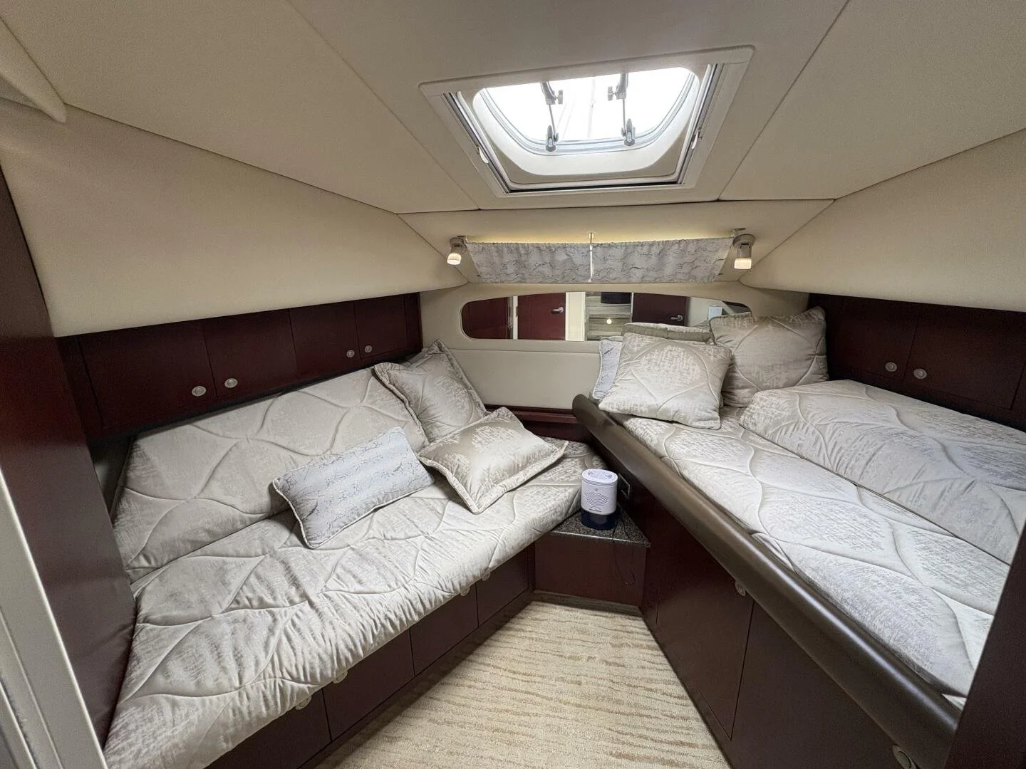 Interior of a boat cabin with two twin beds, pillows, a small table with a speaker, and a skylight on the ceiling.