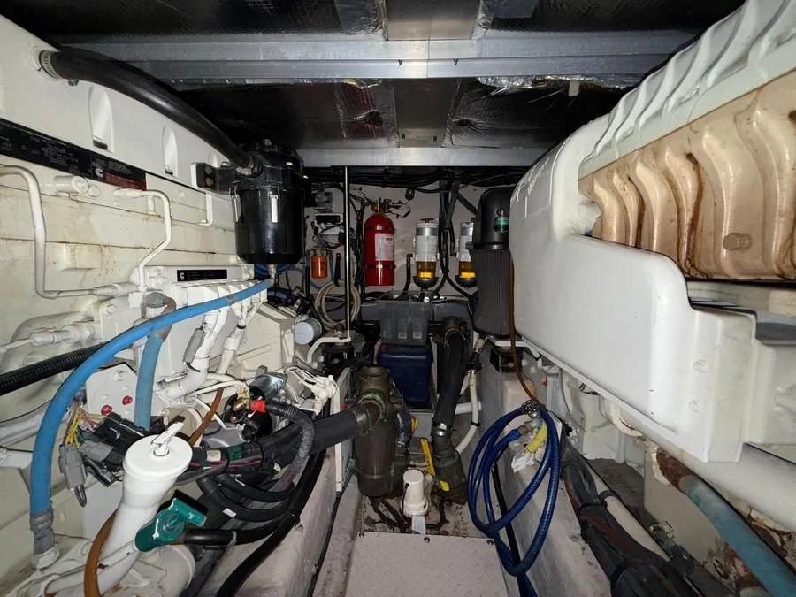 Marine engine room with various pipes, hoses, and equipment, including fire extinguishers and electrical components.