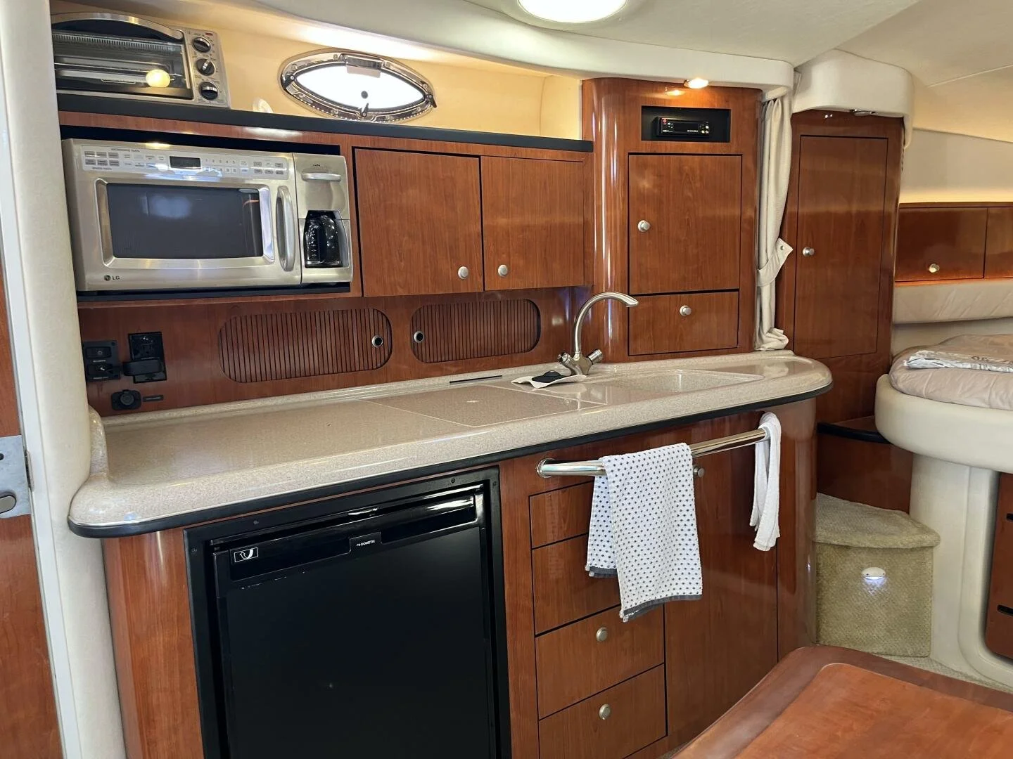 Galley are on Sea Ray 340 Sundancer boat, with cherry wood cabinets, a microwave, a small fridge, a sink with a faucet, and a towel hanging on a rail.