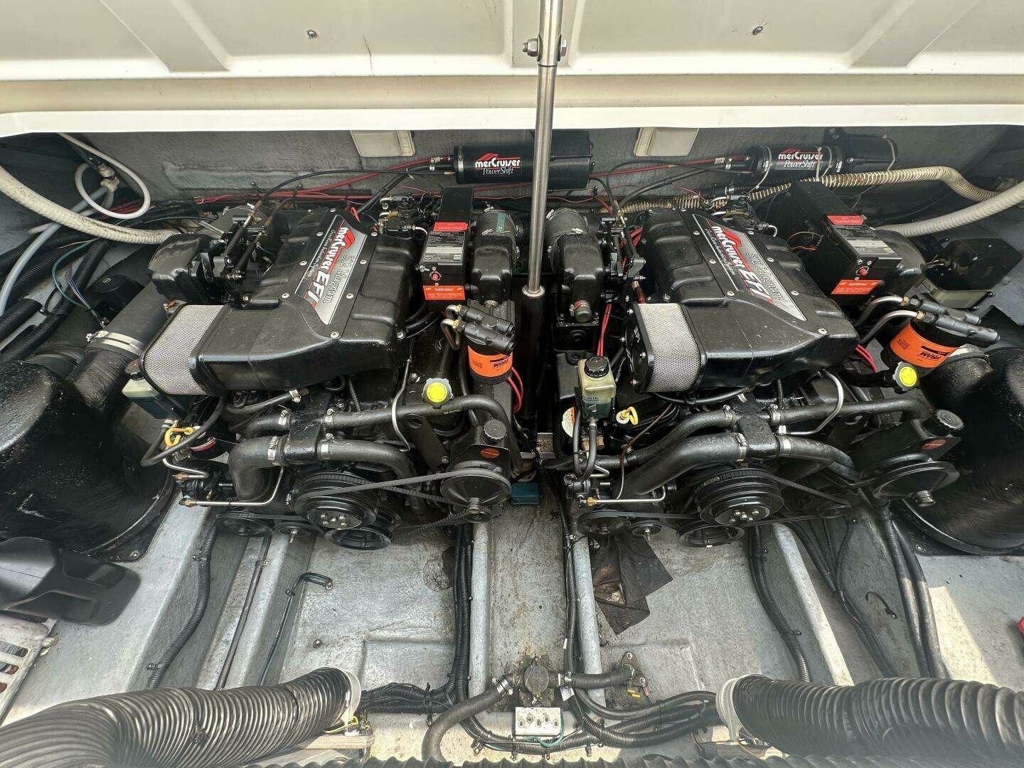 Twin MerCruiser sterndrive boat engines in engine room with black and silver components, hoses, and wiring.
