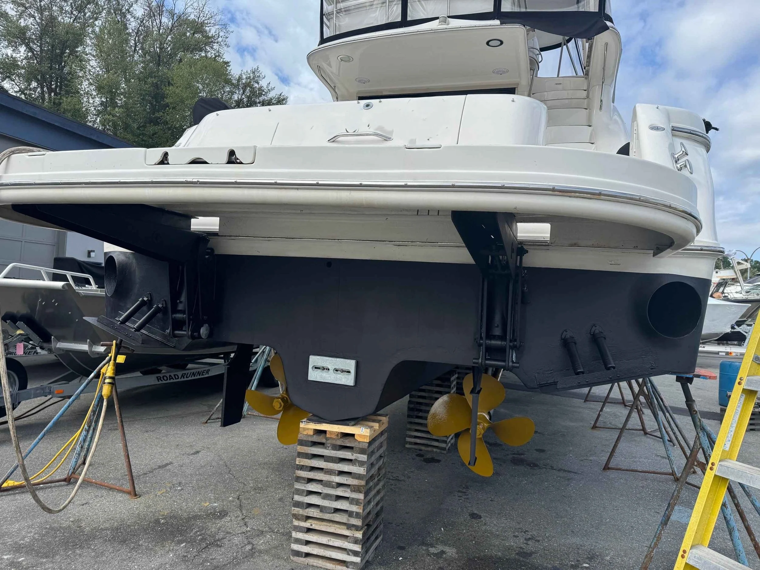 A Sea Ray boat on stands with its black bottom visible, showing two yellow propellers and a large round exhaust port on the side.