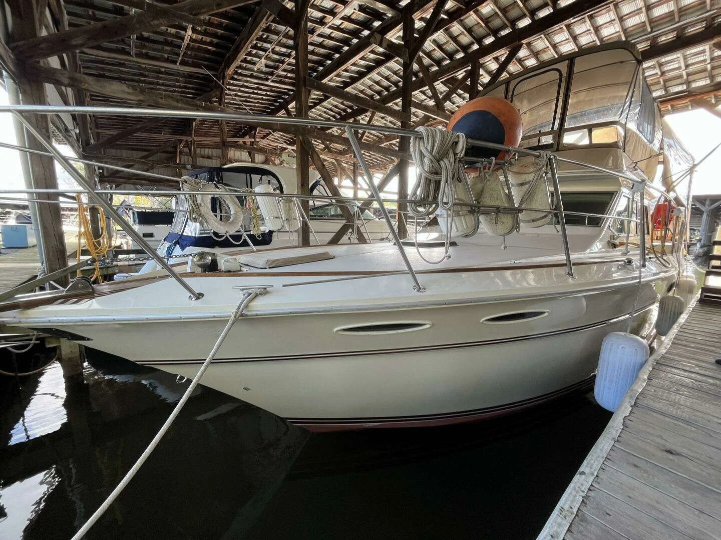 A white Sea Ray motor yacht docked in a wooden covered marina, with ropes, buoys and boat fenders. Aft cabin style Sea Ray 355 Motor Yacht.