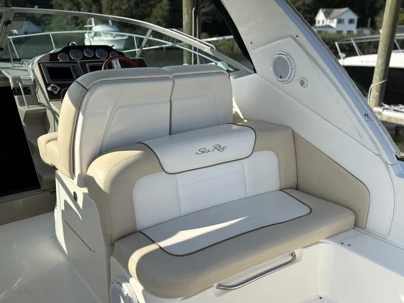 Close-up of the seating area on a white yacht, with a white cushioned bench and a padded backrest that has the logo 'Sea Ray' embroidered on it, near the boat's steering console. Sea Ray 350 Sundancer.