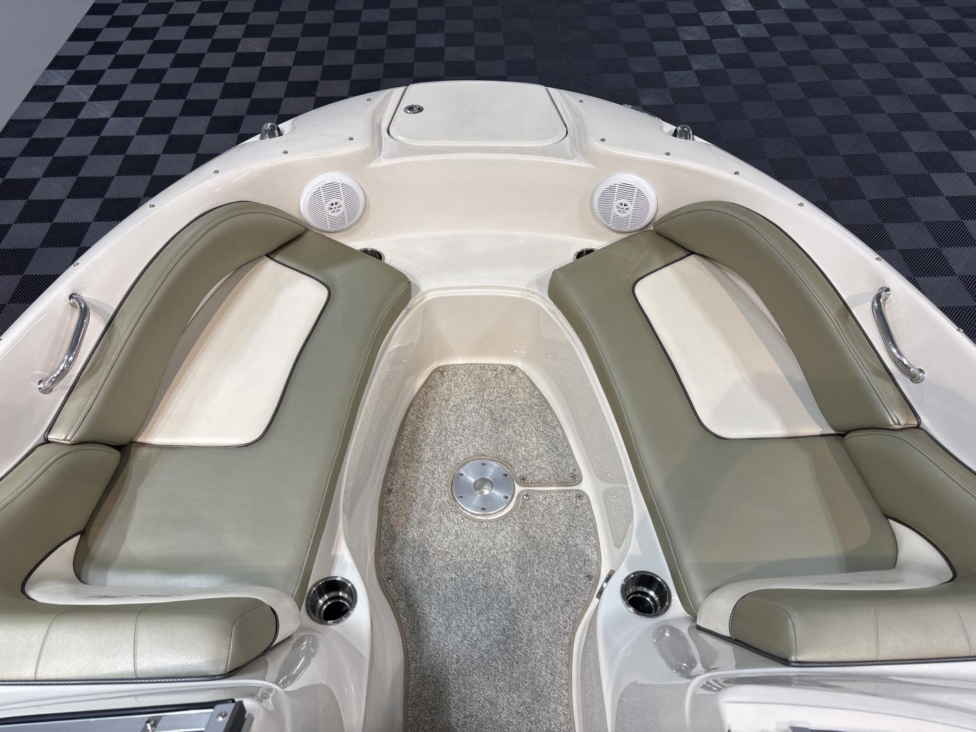 Front bow of a white boat with green cushioned seats, two circular speakers, and a small hatch, on a checkered black and gray background.