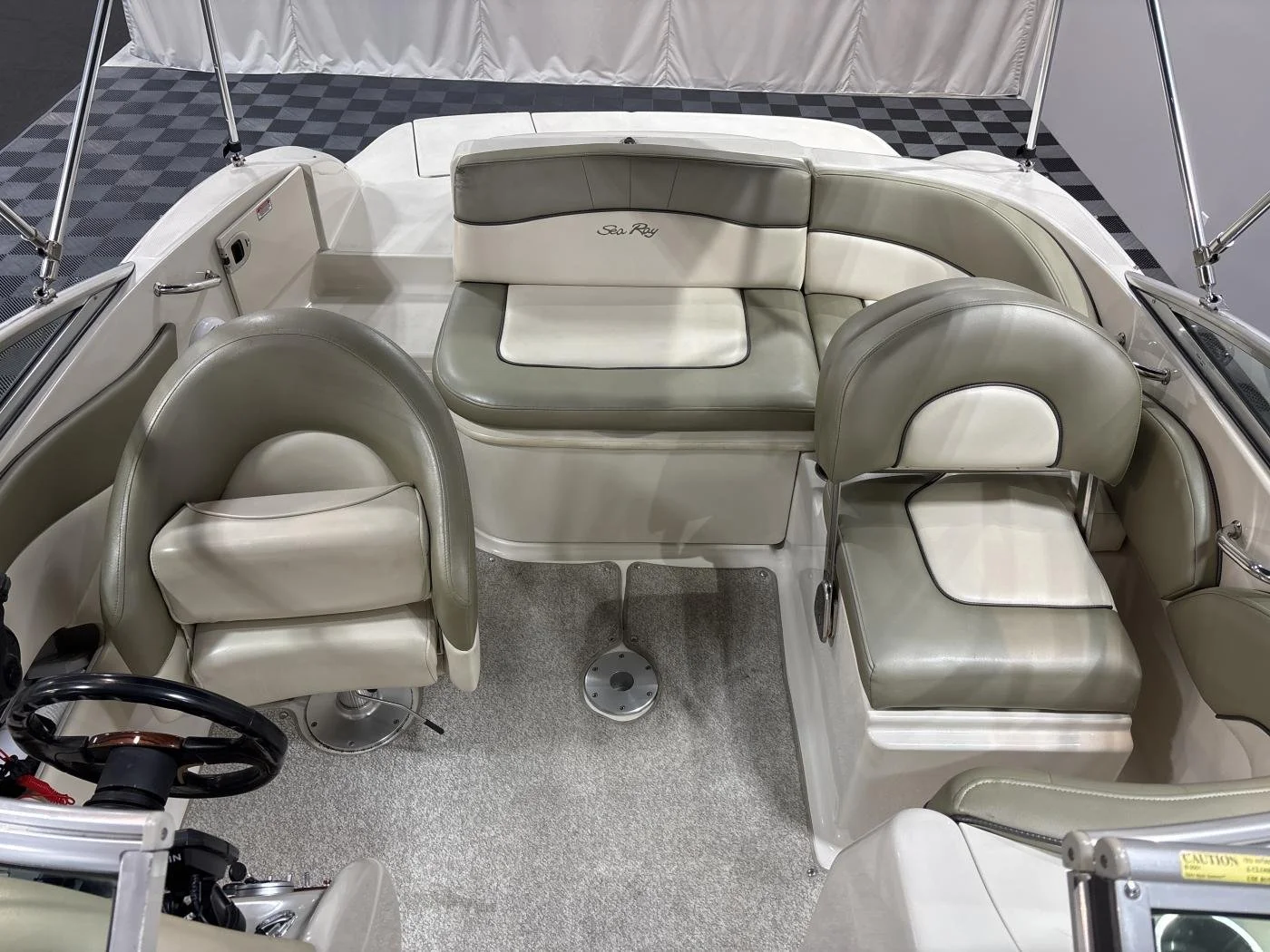 Interior of a beige and white pontoon boat with multiple cushioned seats and a steering wheel.