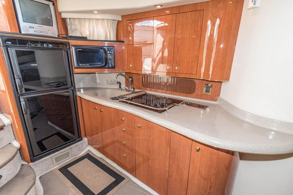 Kitchen area inside a boat with wooden cabinets, a microwave, a mini refrigerator, a small TV, a sink, a gas cooktop, and a curved countertop.