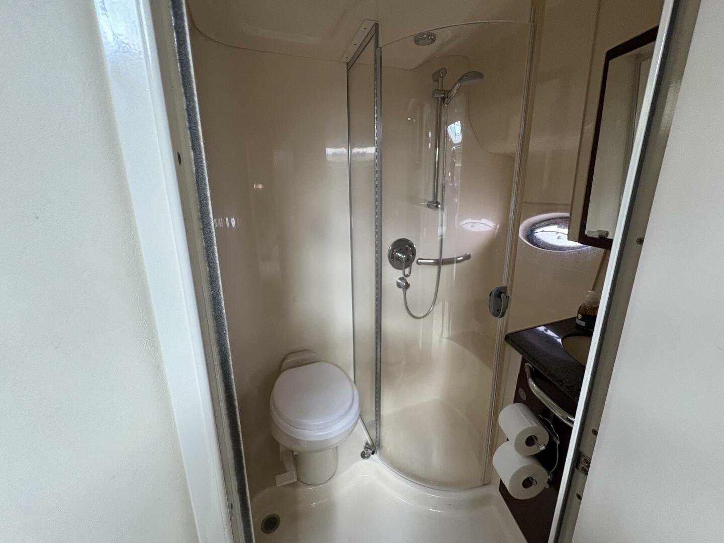Small bathroom with a toilet, a shower with a glass enclosure, and a small sink with a mirror and two toilet paper rolls, on a Sea Ray yacht.