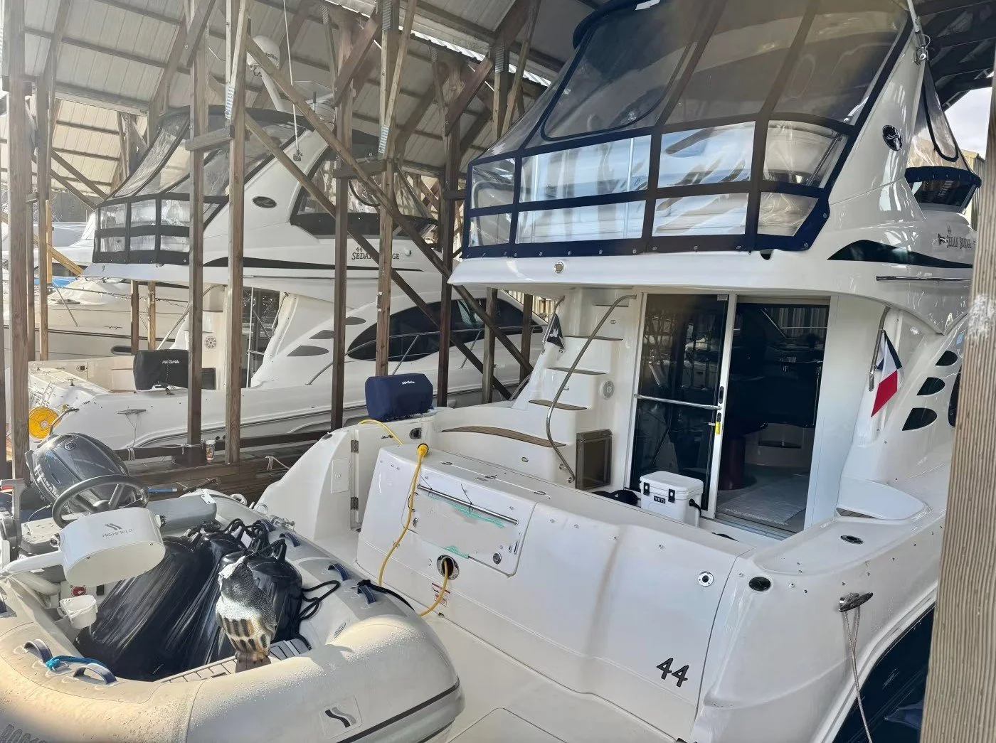 A pair of Sea Ray boats stored in a covered boat shed, including a large white yacht with a flybridge and an inflatable dinghy in the foreground.