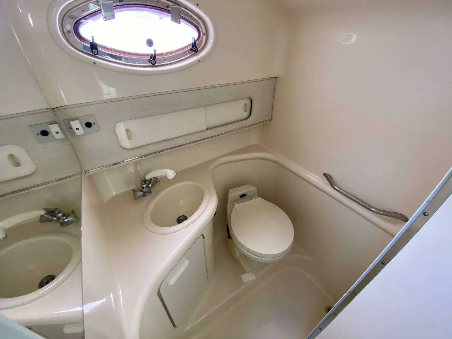 Compact washroom head area with sink, a toilet, a window, and mirrors, with beige-colored fixtures and walls. Sea Ray 270 Sundancer.