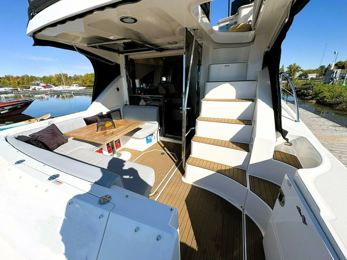 Luxury yacht with outdoor seating area, wooden steps, and harbor in the background.