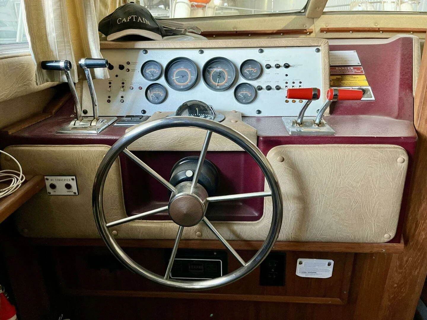 The image shows the helm and control panel of a boat with steering wheel, throttle controls, and various gauges, with a black captain's hat on top of the panel.