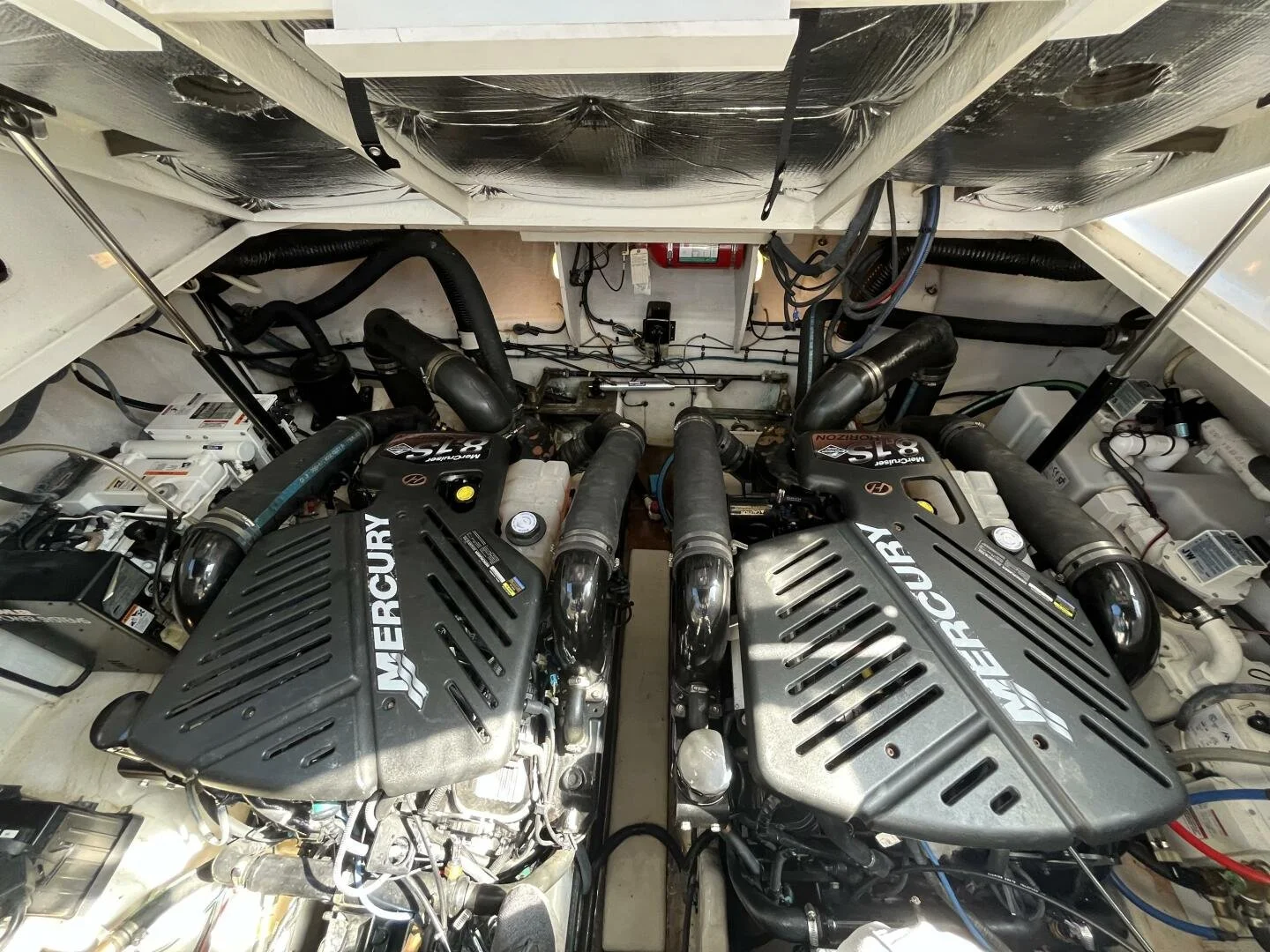 Two Mercury MerCruiser gasoline engines, Sea Ray 340 Sundancer boat engine room, with various hoses, wires, and mechanical components visible.