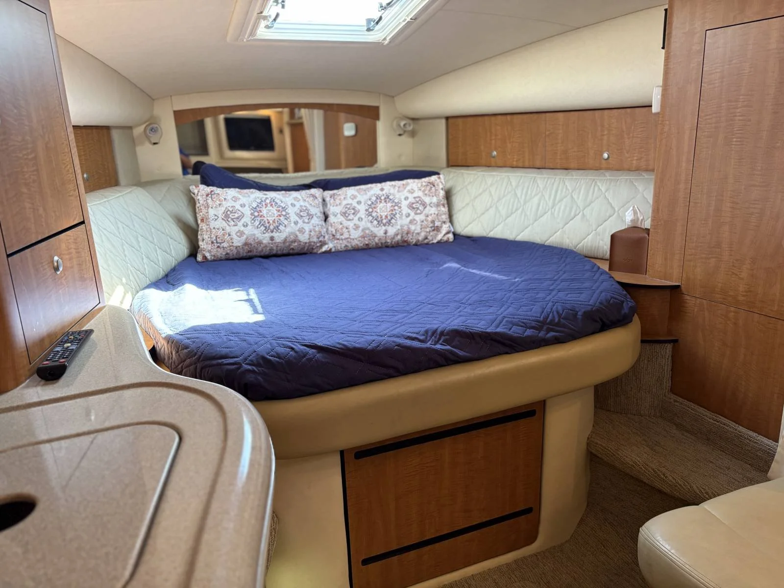 A cozy bedroom on a Sea Ray boat, with a round bed, blue quilt, and decorative pillows.