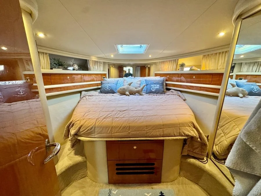 A cozy bedroom inside a boat or yacht with a large bed, pillows, and a plush dolphin toy, with a skylight on the ceiling and mirrors on the sides. Forward stateroom, Sea Ray 480 Sedan Bridge.