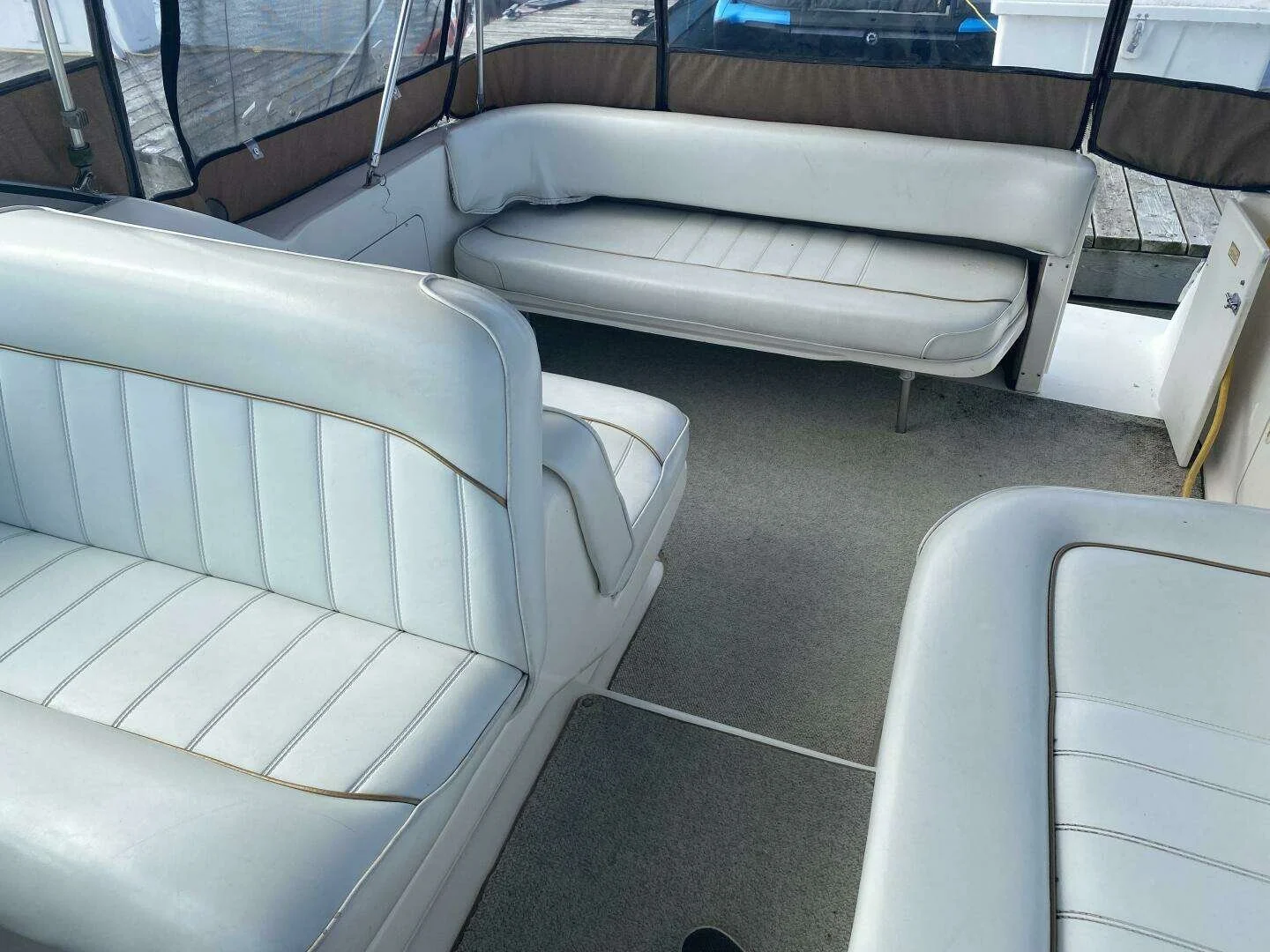 Interior of a boat with white cushioned seating and a beige fabric surround, gray carpeted floor, and nearby parked vehicles visible through the windows. Express style Sea Ray 270 Sundancer boat.