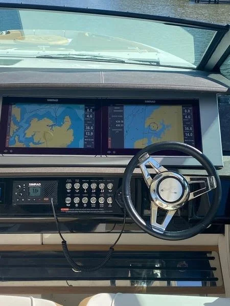 Boat dashboard with two marine navigation screens displaying a sea map, a control panel with various buttons, and a steering wheel.
