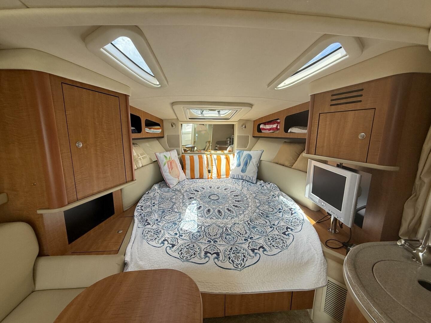 Interior of a yacht cabin with a round bed, decorative pillows, small television, skylights, and wooden cabinetry.