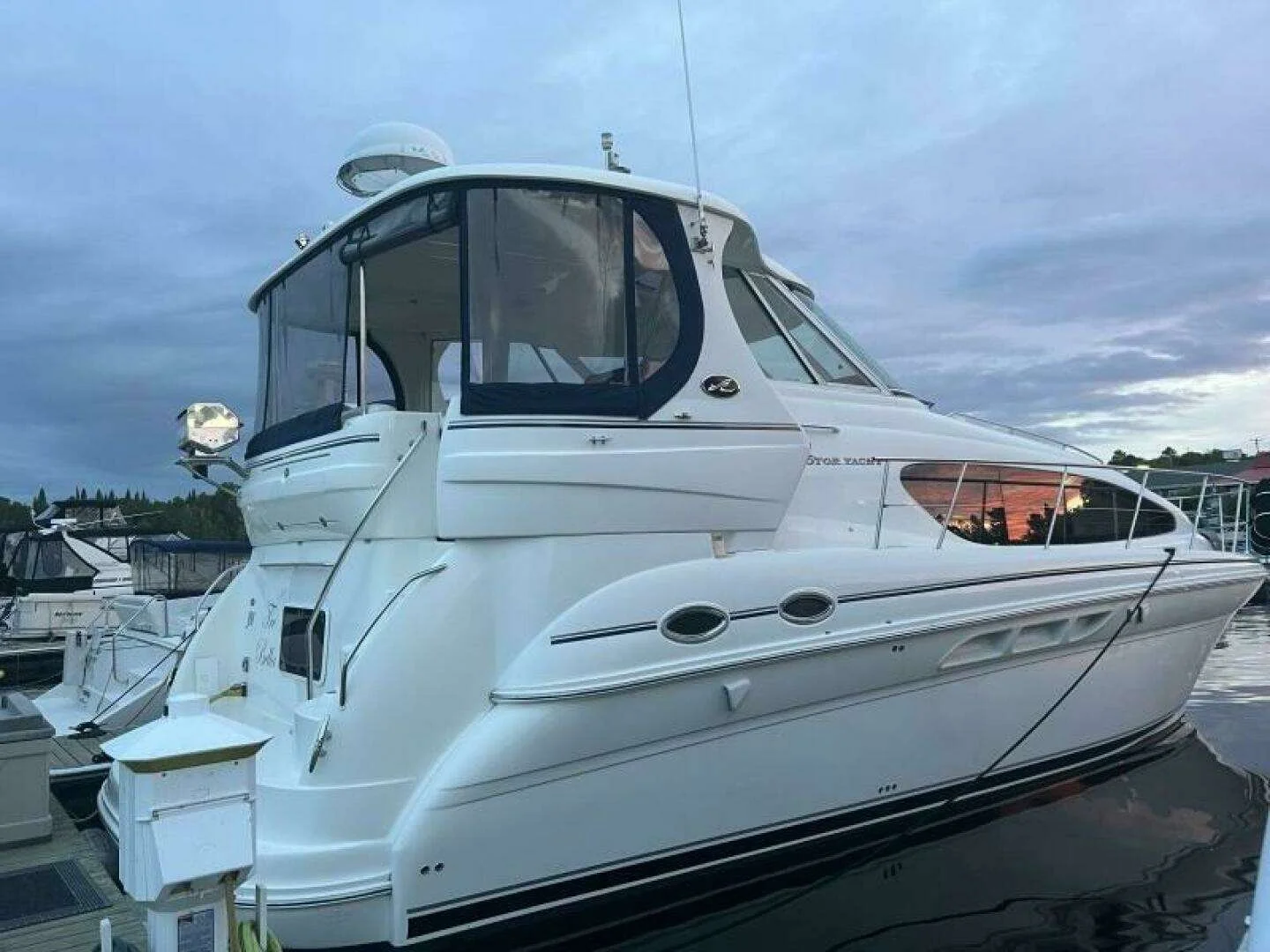 A white yacht docked at a marina during dusk with a cloudy sky in the background.