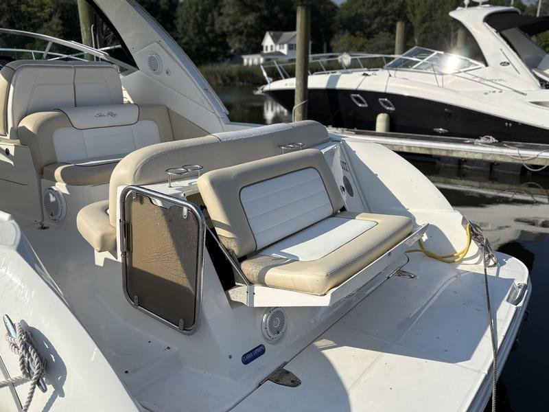 View of the back deck of a white yacht with beige cushioned seating, docked at a marina with other boats in the background. Sea Ray 350 Sundancer.