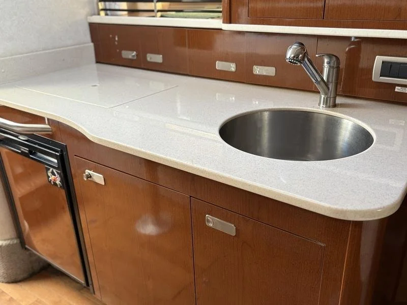 Kitchen countertop with dark wood cabinets, a built-in sink with a faucet, and a small refrigerator.